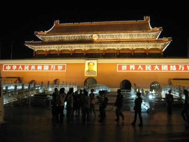 Tiananmen Gate lit up at night with Mao's portrait and red banners, people standing in front