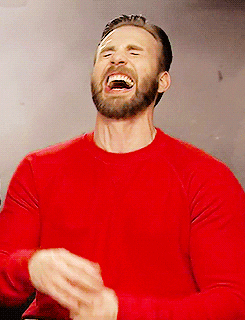 Bearded man in a red sweater laughing hard with his head tilted back