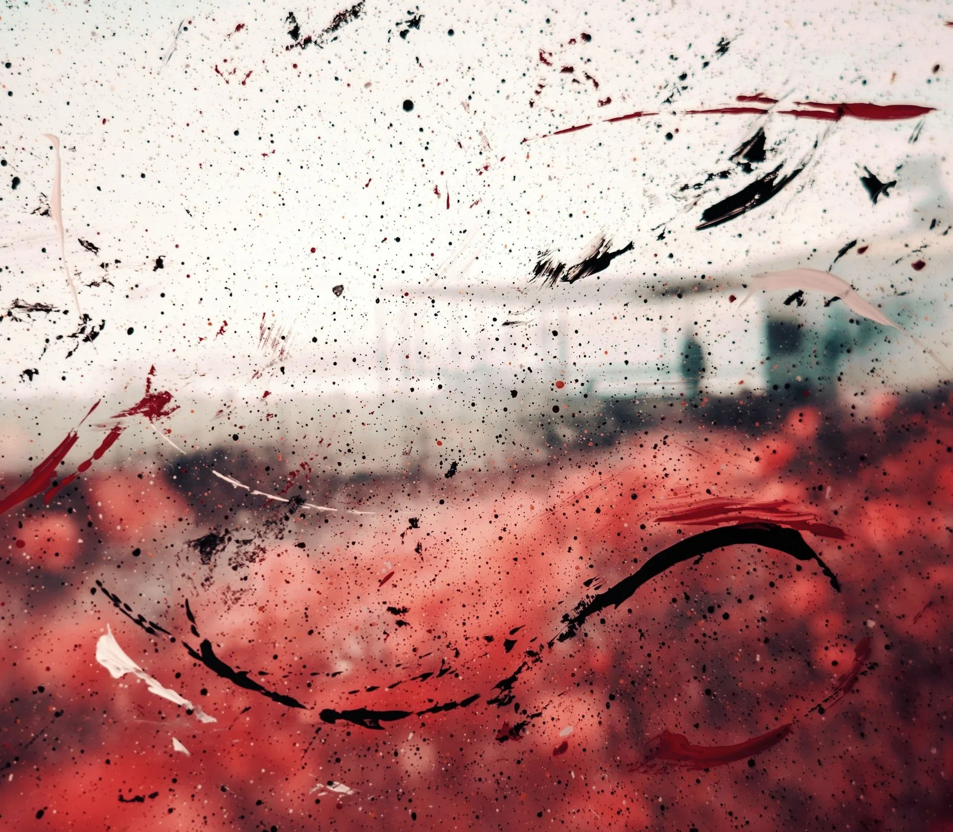 Close crop of paint splatters in black, red and white on glass over a blurred red and grey scene