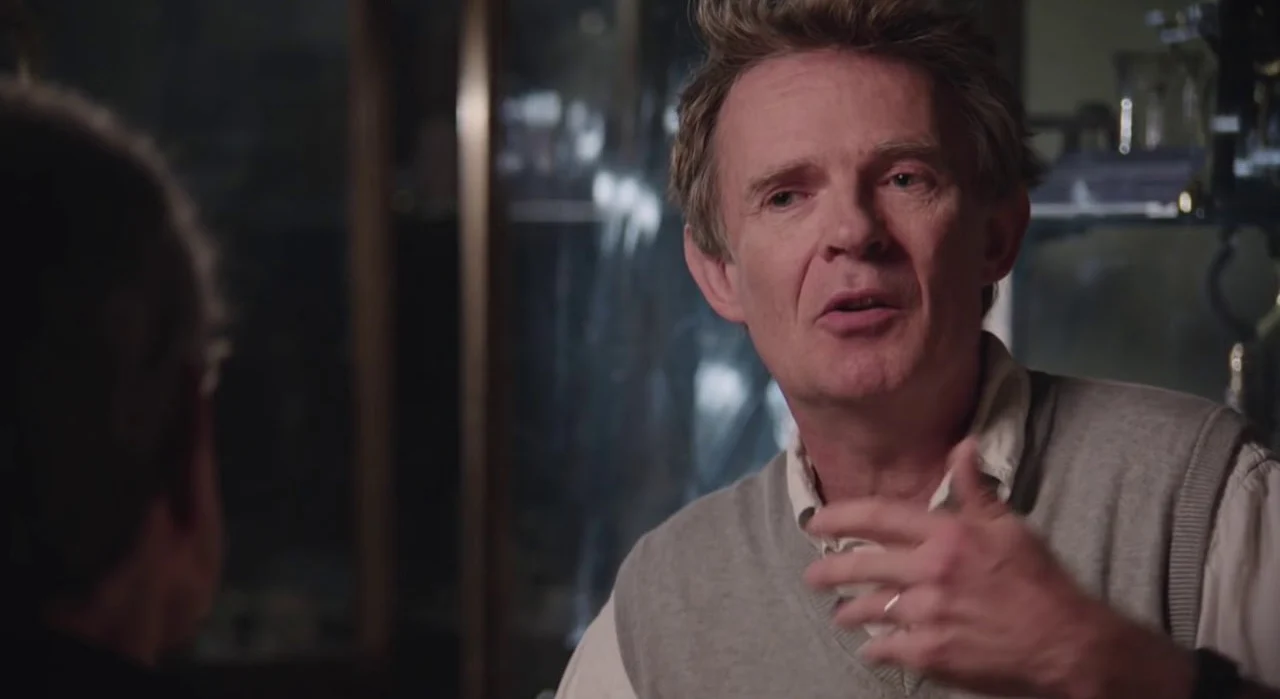 Galen Strawson, a man in a gray sweater vest, talking and gesturing during an interview