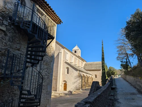 Spiral iron staircase on a stone building with the abbey church and a tall cypress beyond