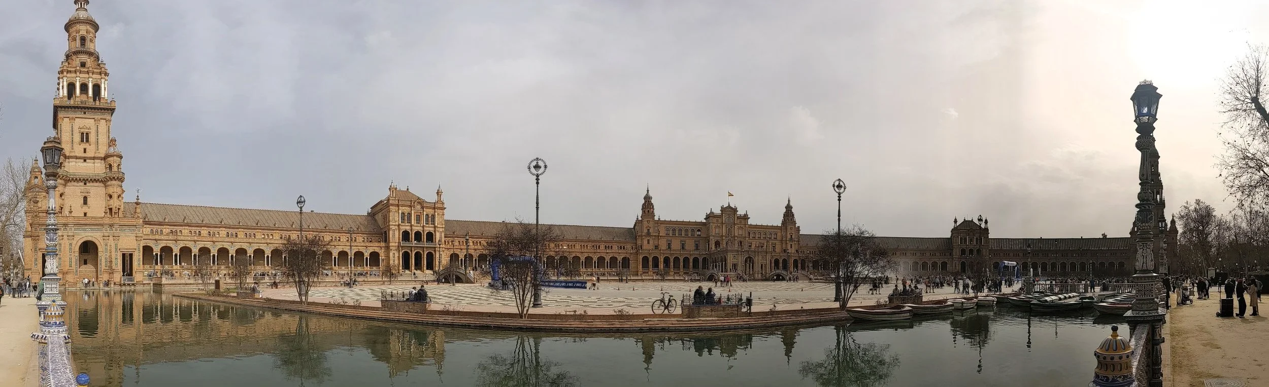 Panorama of Plaza de Espana in Sevilla, a long brick building with towers curving around a canal