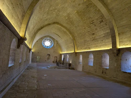 Long vaulted stone hall lit warmly from below, with a round window at the far end