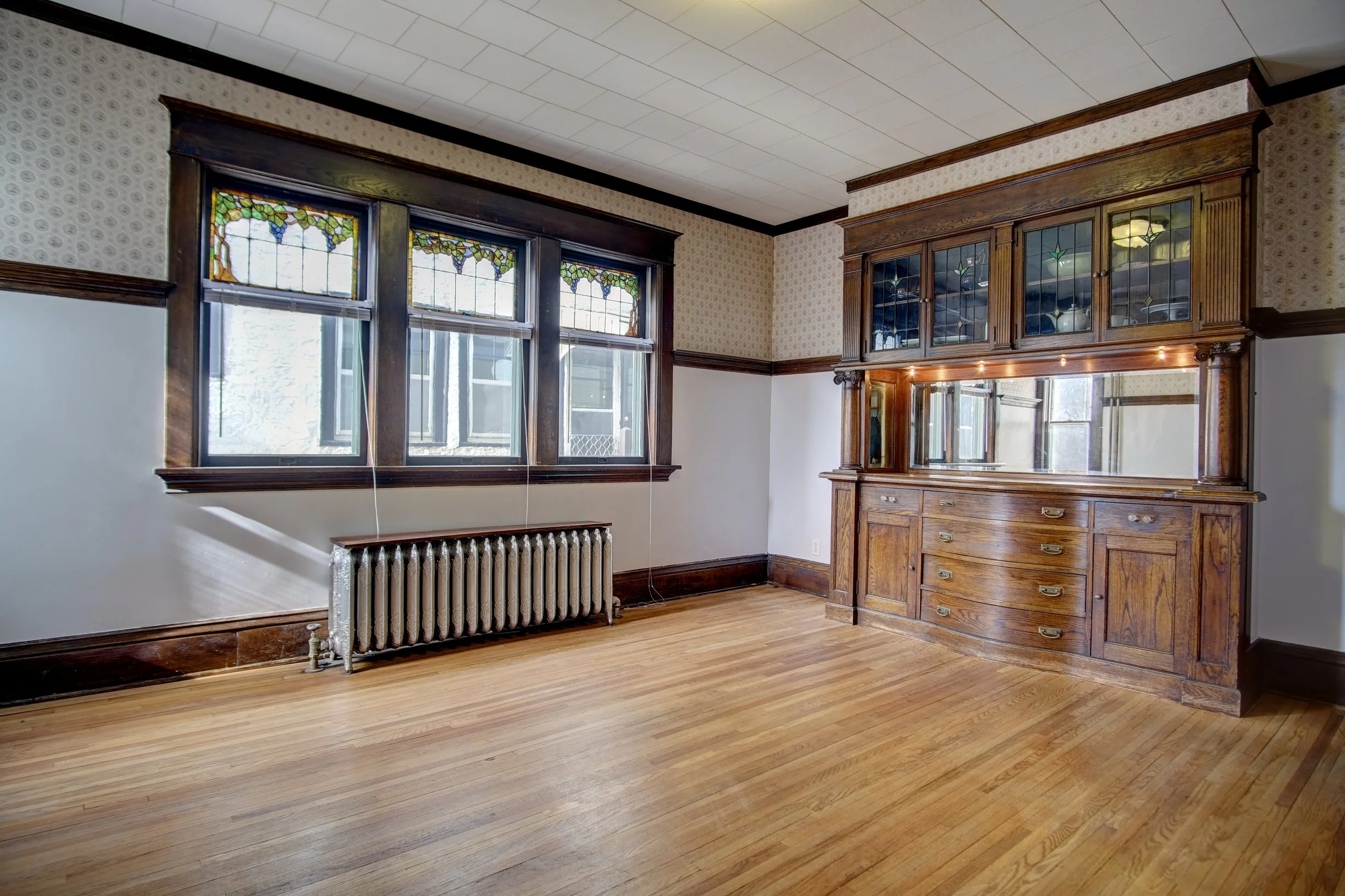 Empty dining room with stained glass windows, a radiator, wood floors and a built-in oak buffet