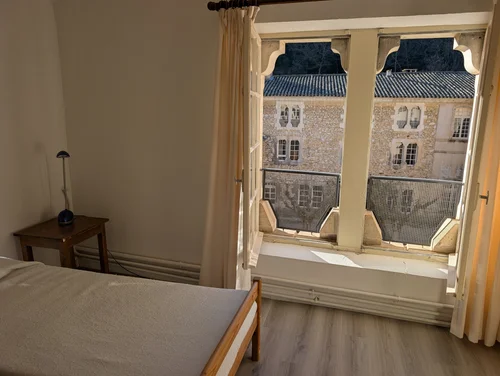 Simple guest room with a bed and small lamp, its window looking out on an old stone building