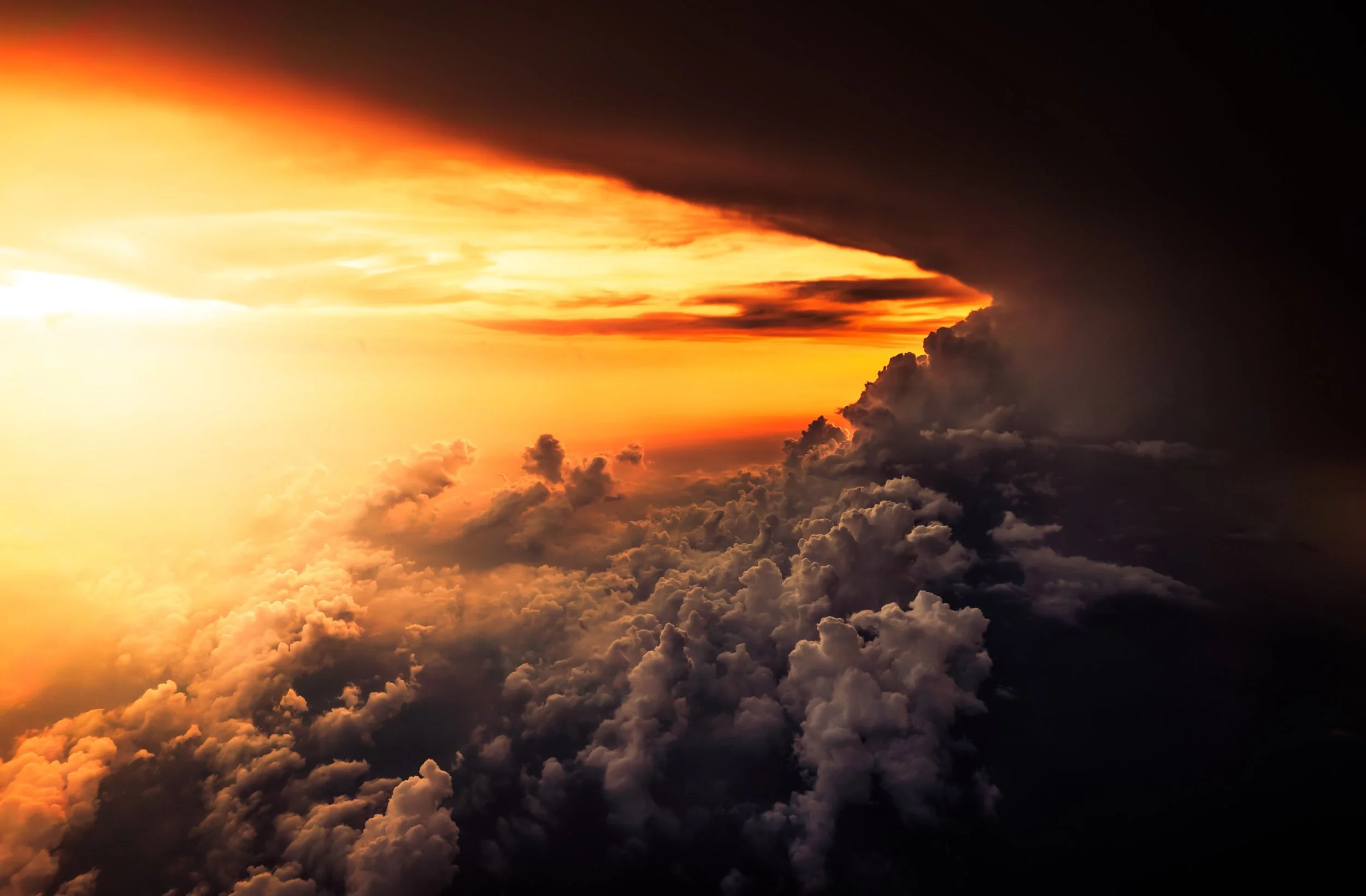 View above the clouds with bright orange sunlight breaking through dark storm clouds