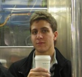 A young man holding a paper coffee cup sits on a subway train
