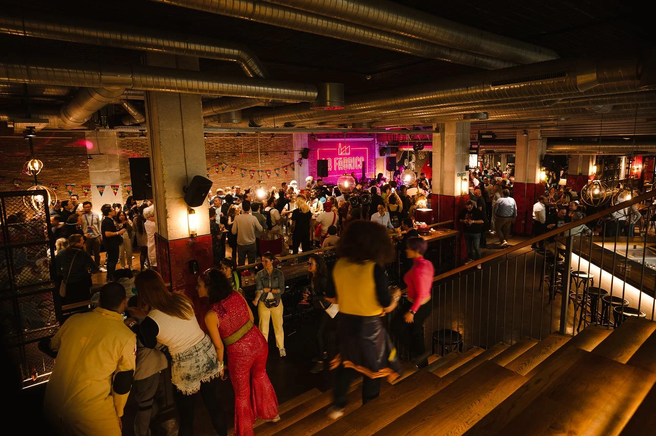 Crowded, dimly lit venue with exposed ducts and a pink neon sign during a conference evening event