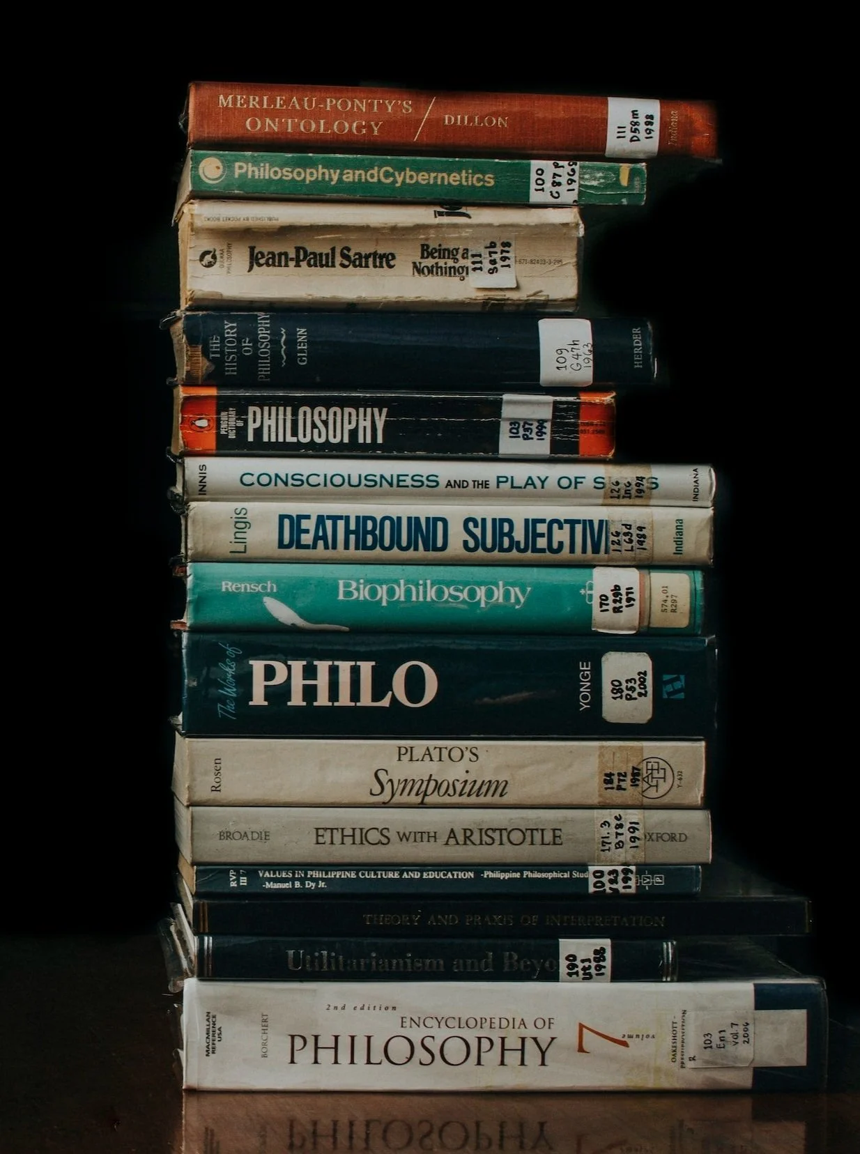 Tall stack of worn library philosophy books, including Sartre, Plato's Symposium and an encyclopedia of philosophy