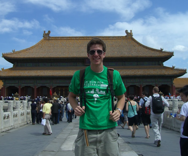 A young man in a green T-shirt and sunglasses smiling in front of a palace hall in the Forbidden City