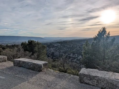 View from a roadside overlook across a wooded valley and distant hills as the sun sets
