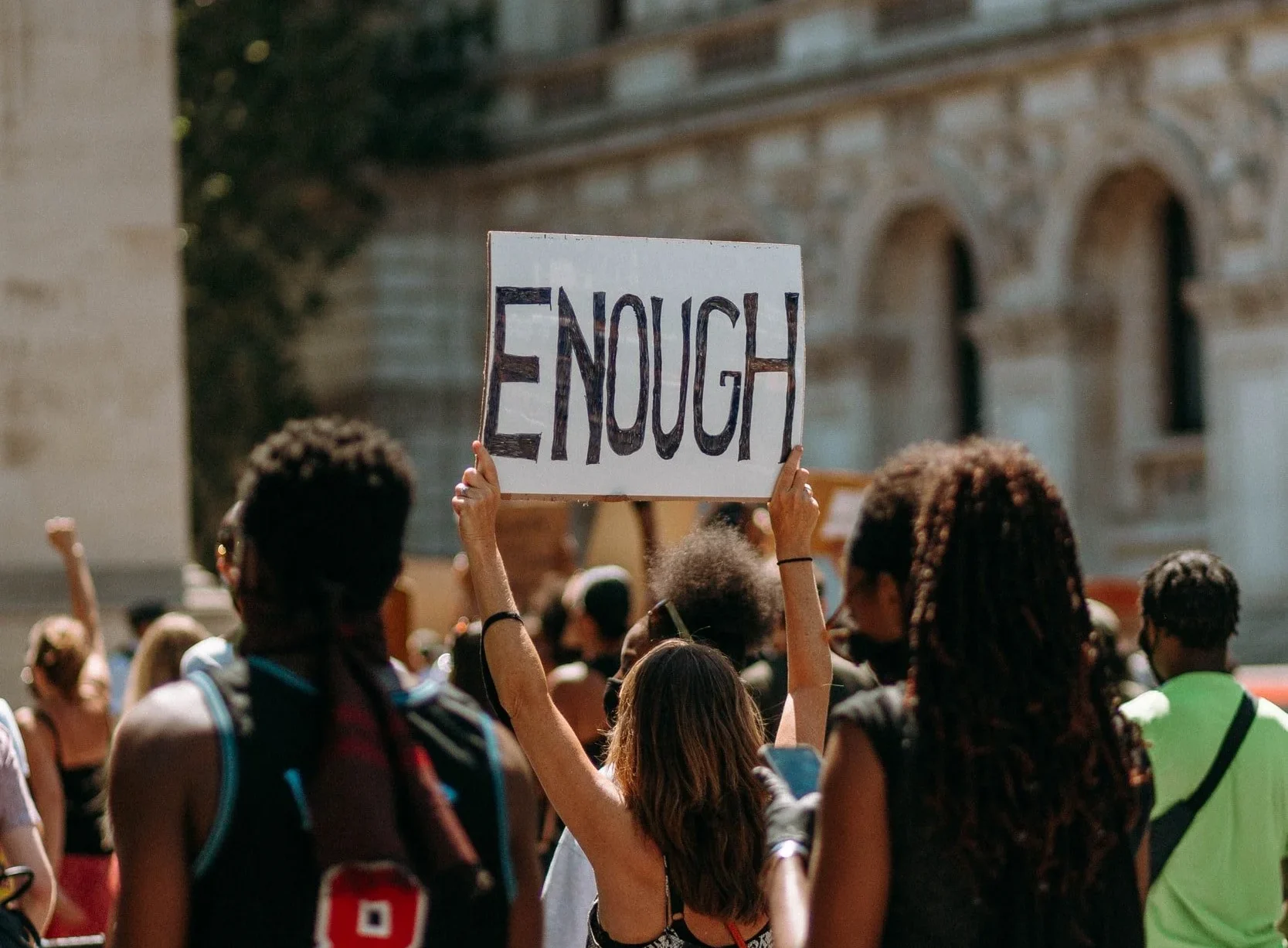 A protester in a crowd holds up a handwritten sign reading ENOUGH