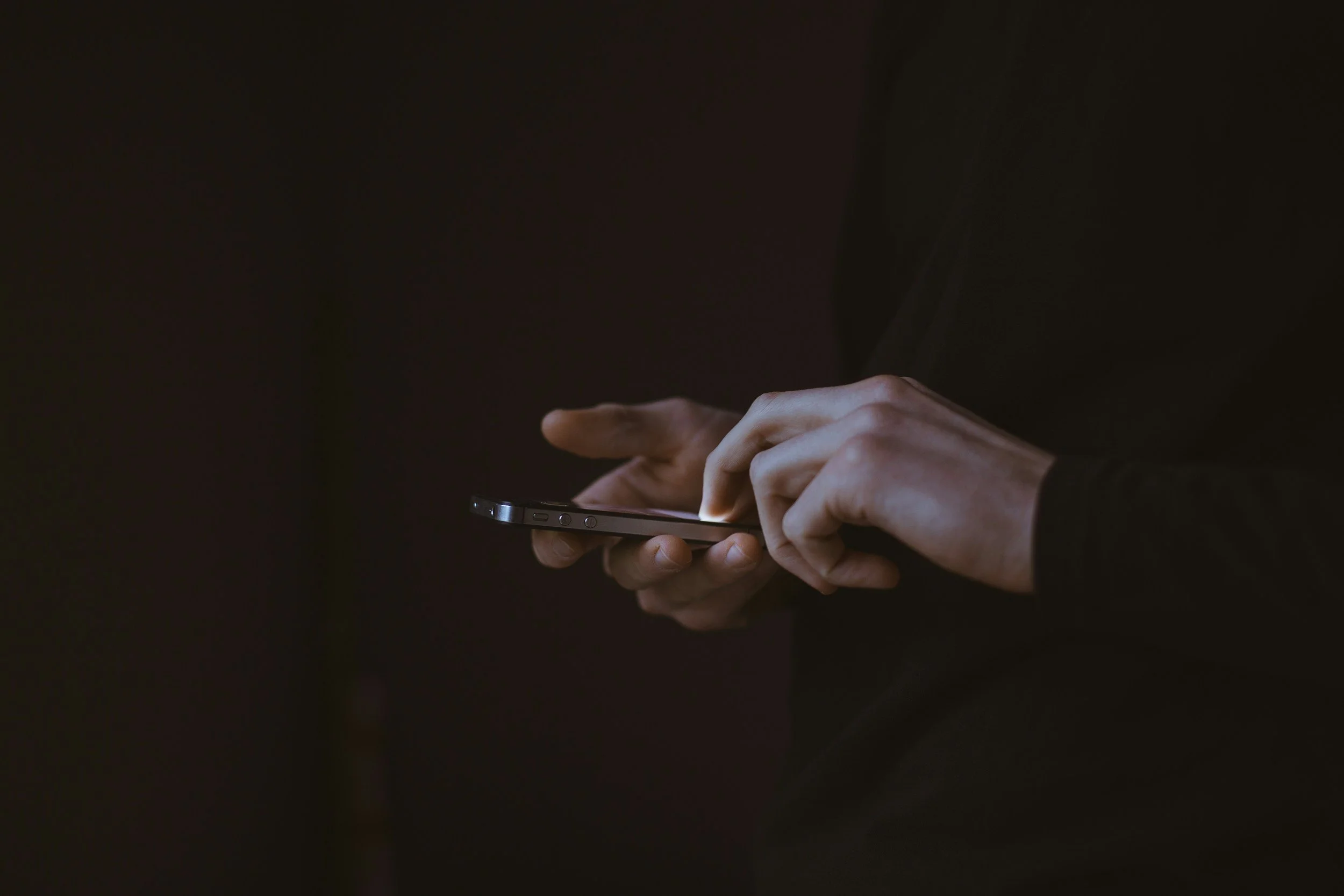 Close-up of hands tapping a glowing smartphone screen in a dark room