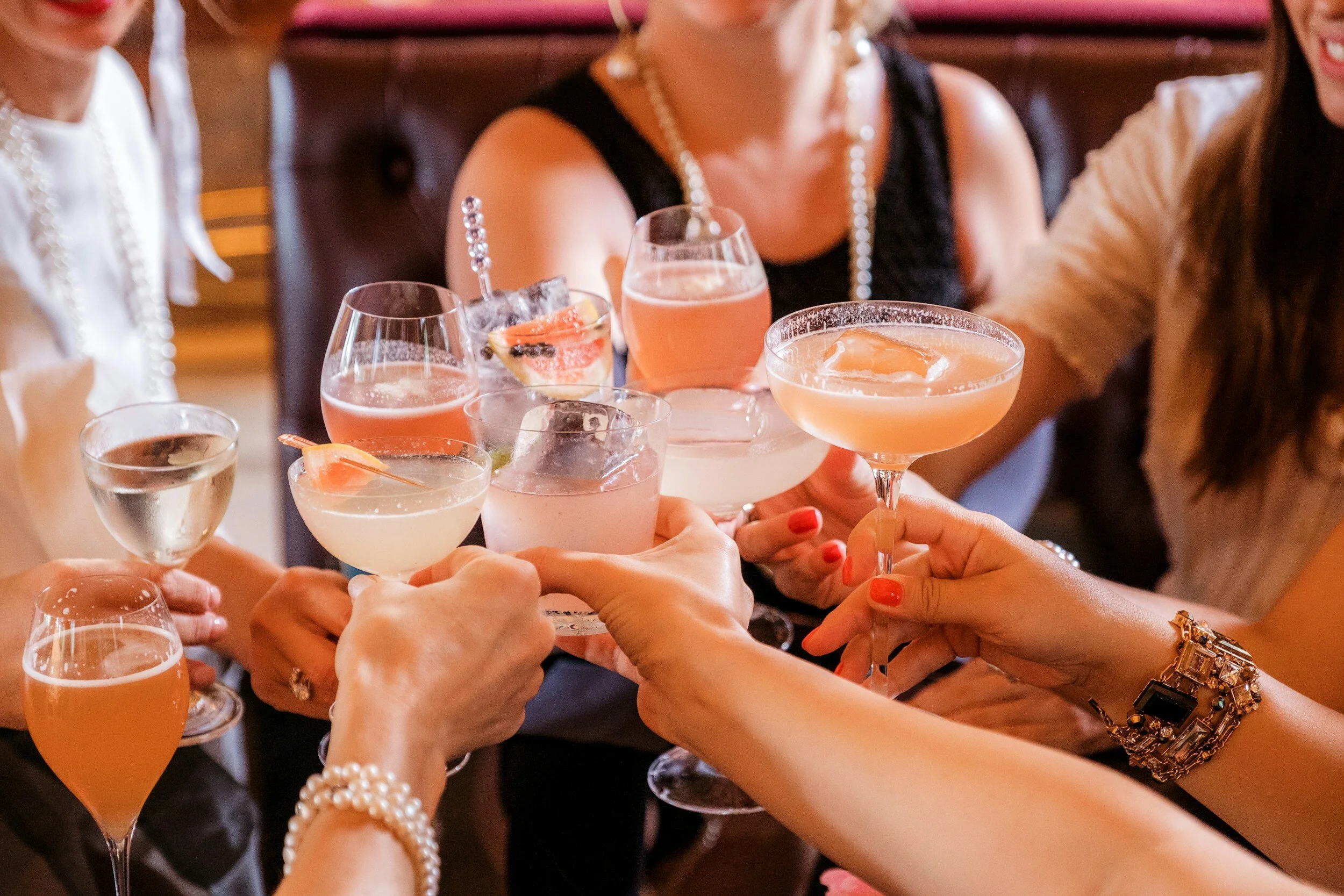 A group of women clinking glasses of colorful cocktails together