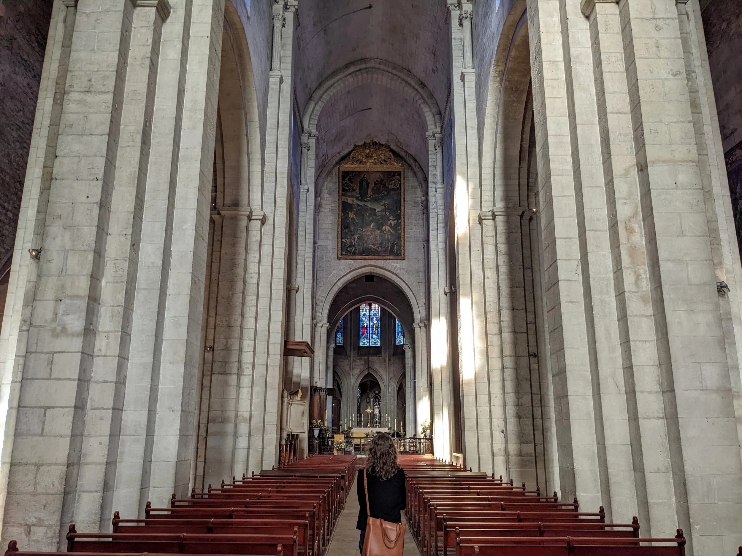 Woman with curly hair walking down the aisle of a tall stone church toward the altar and stained glass
