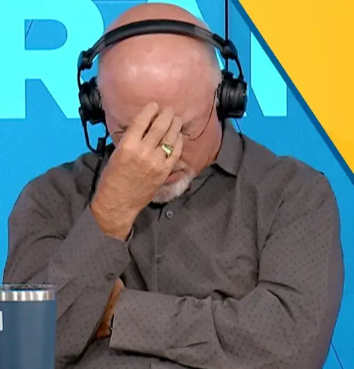 Bald man with a white beard and headphones covering his face with his hand in a radio studio