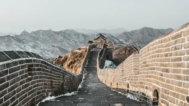 The Great Wall of China winding over snow-dusted mountains toward a stone watchtower